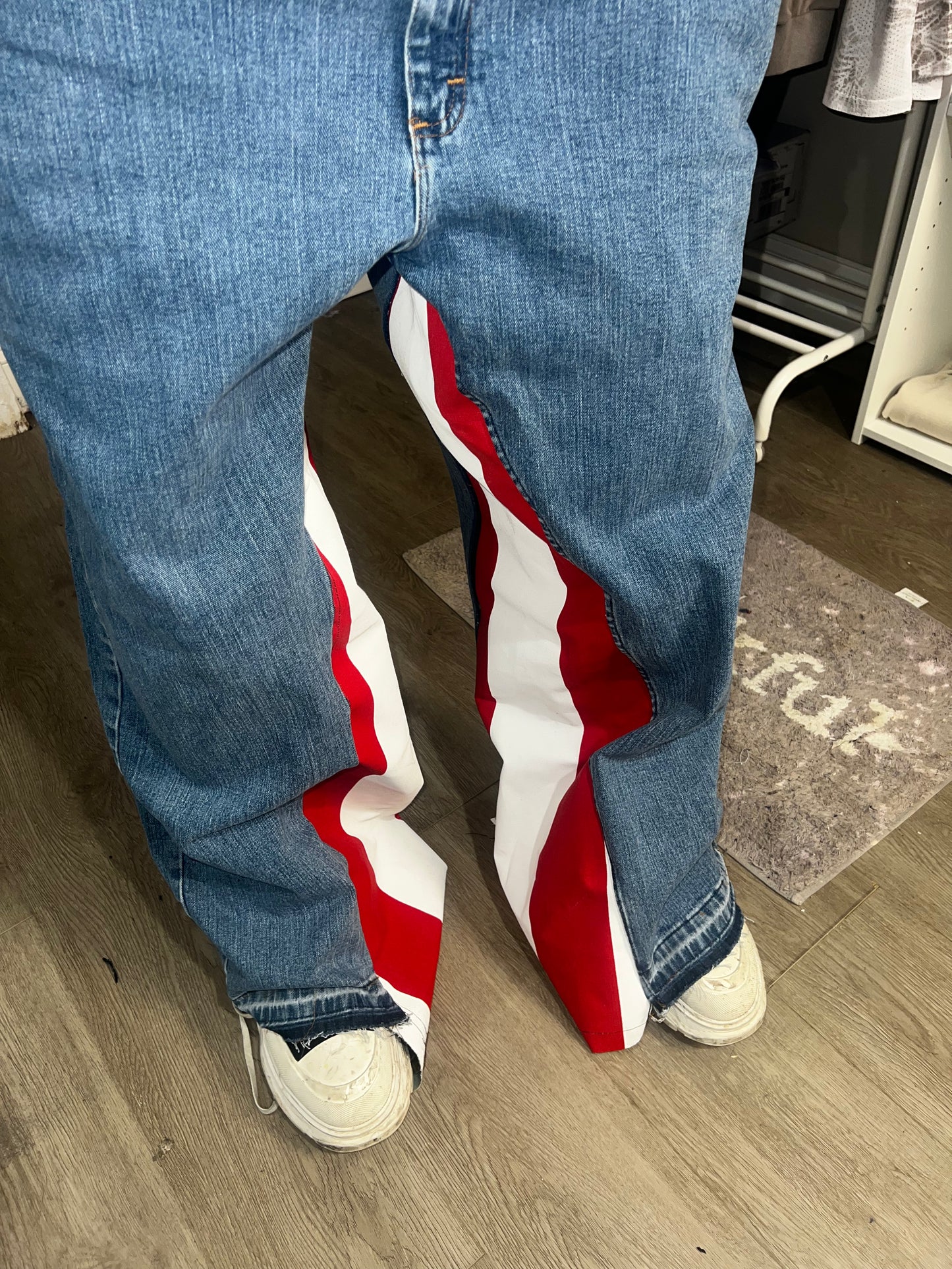 Person wearing blue jeans and red, white, and blue sneakers on a wooden floor.