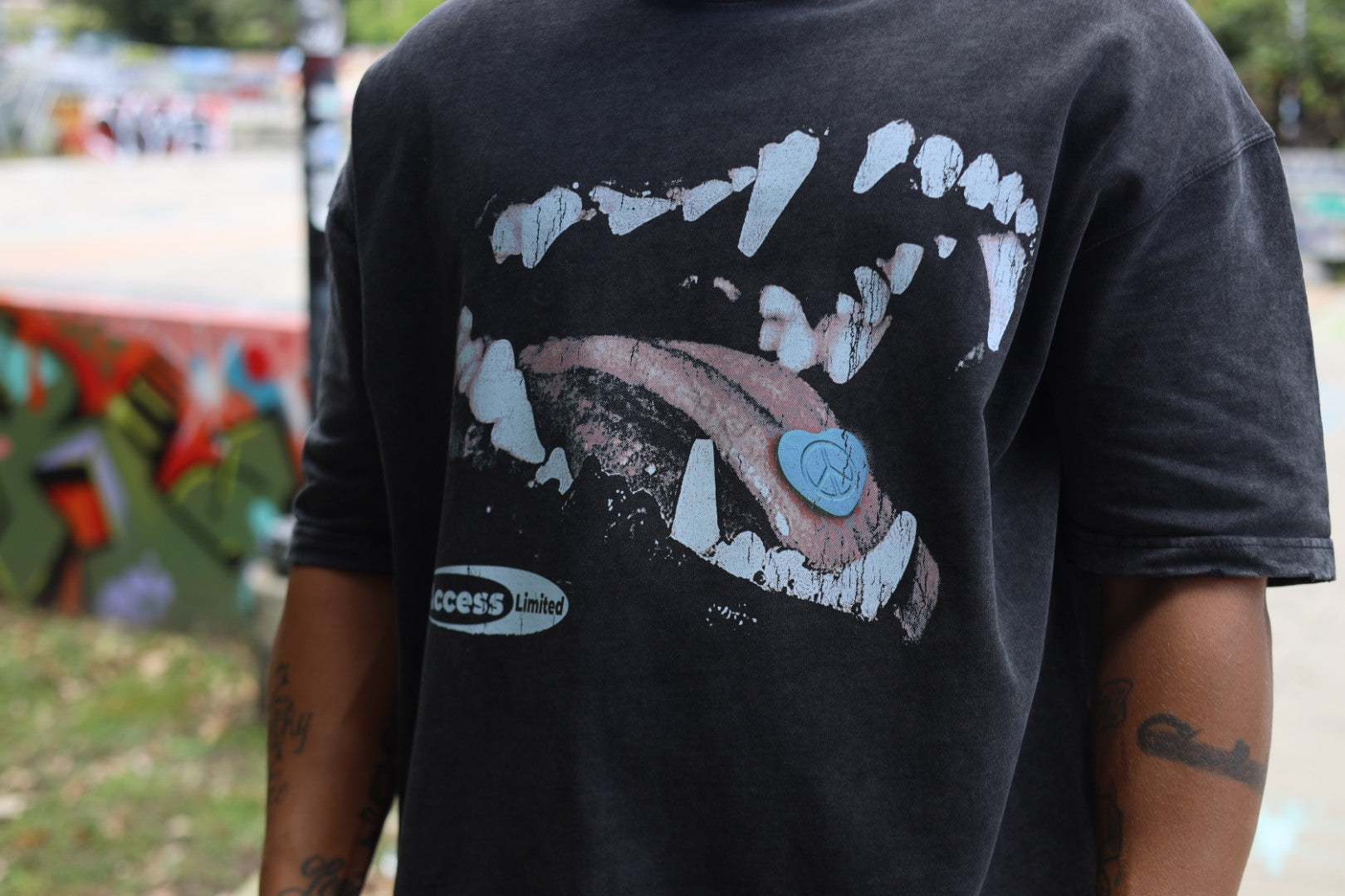 The Bite “Protect Inner Peace” Graphic Tee featuring a graphic of fangs and tongue detail on a black washed tee.