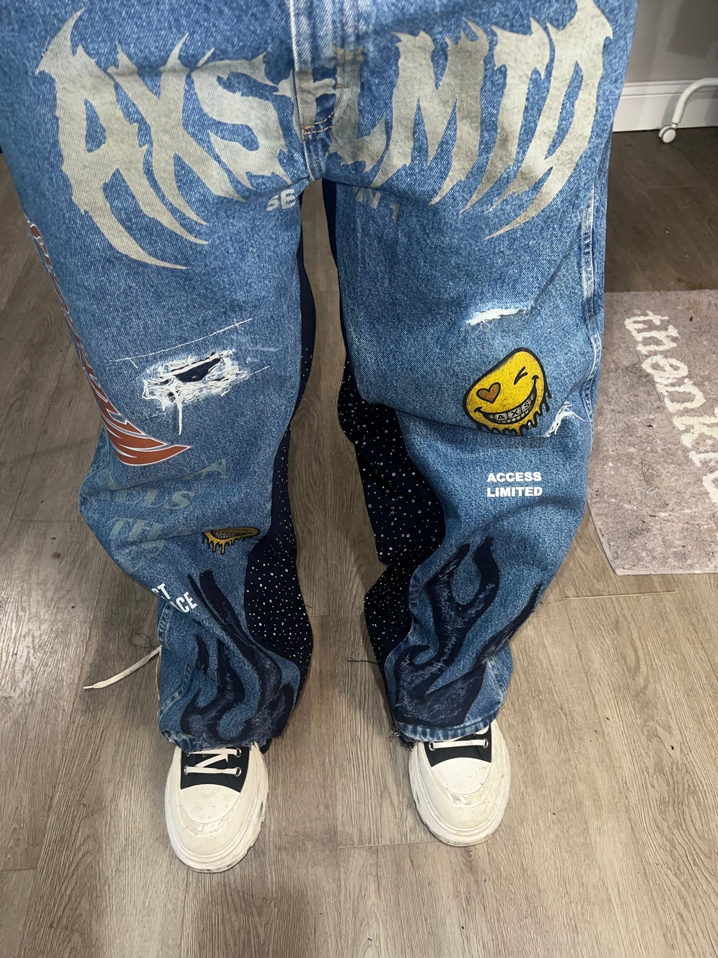 Blue jeans with graphic designs and text on a wooden floor.