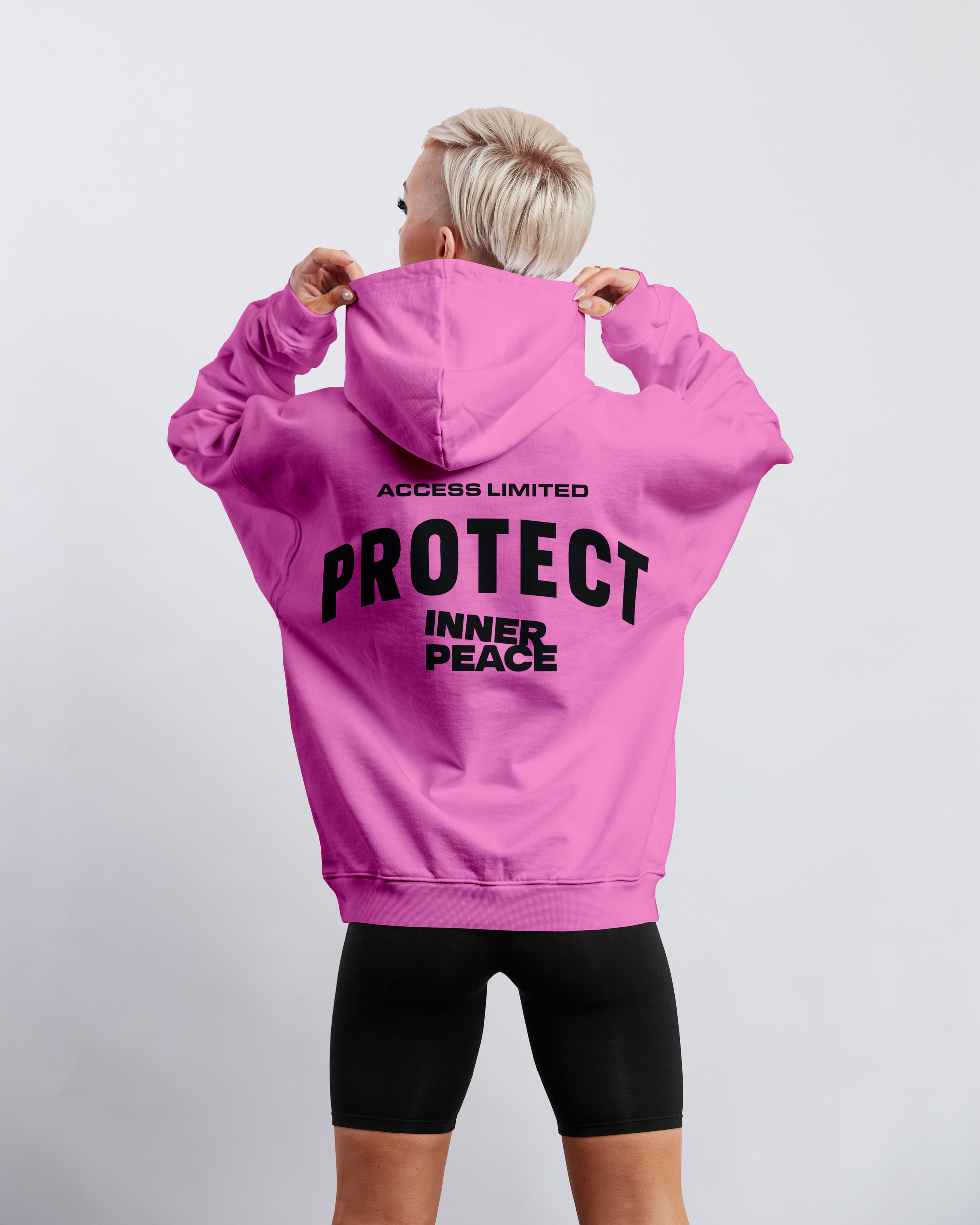 Person wearing a pink hoodie with Access Limited Protect Inner Peace text on the back against a white background